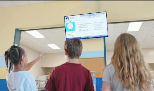 Kids looking up at menu display screen in school lunchroom
