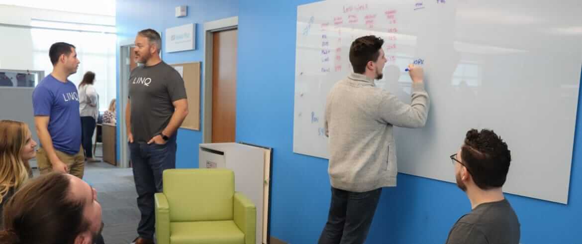 LINQ team members collaborating in a brainstorming session while one employee is writing ideas on a whiteboard on the wall