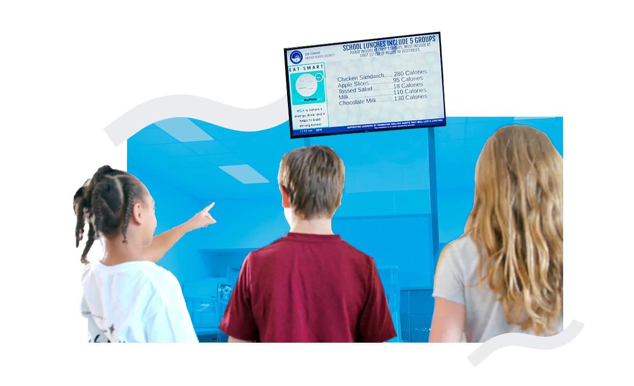 Elementary students in the lunchroom reading and pointing at a digital menu display