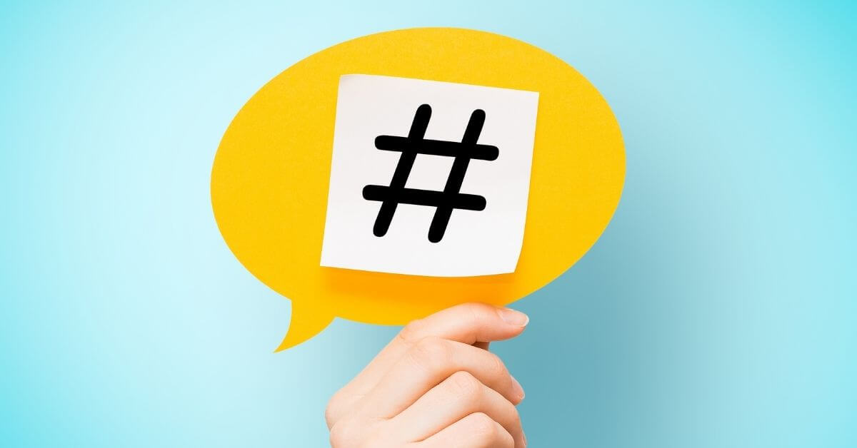 Human hand holding up a yellow speech bubble with a black hashtag mark inside a white square in front of a blue background education influencers on twitter