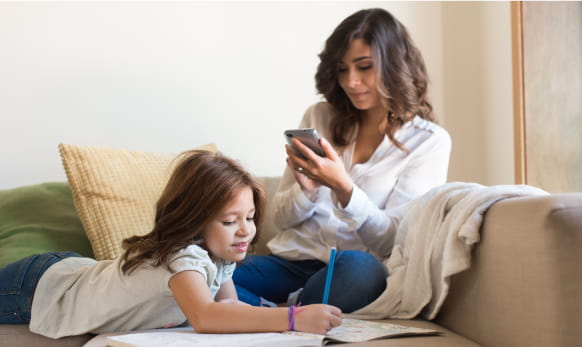 Parent looking at smartphone while daughter does homework.