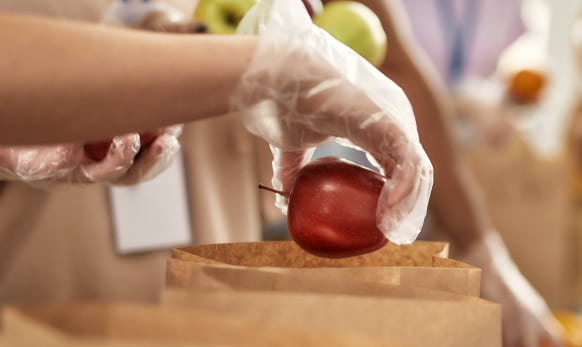 Foodservice worker dropping an apple into a bag